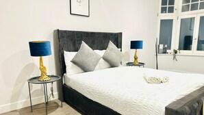 A bedroom with a large bed, two bedside tables with lamps, a window with curtains, and a framed picture on the wall. - Spacious Margate Apartment- Beach,arts&high Street (Margate)