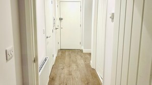 A narrow hallway with white walls and wooden flooring, leading to a closed door at the end. - Spacious Margate Apartment- Beach,arts&high Street (Margate)