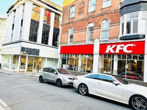 Ein KFC Restaurant mit rotem Schild, neben einem Gebäude mit großen Fenstern und heller Fassade.
