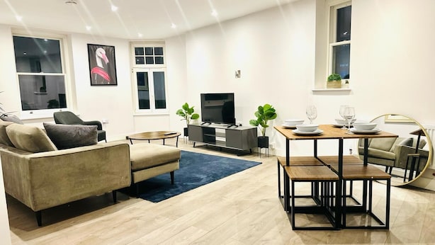 A modern living room with a sofa, TV, dining table, and a blue rug. - Spacious Margate Apartment- Beach,arts&high Street (Margate)