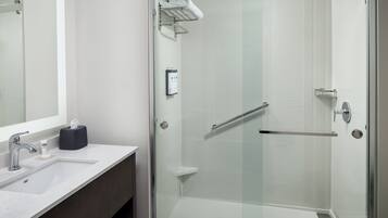 Ein modernes Badezimmer mit einer Duschkabine, einem Waschbecken mit Handtuchspender und einem Spiegel.