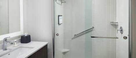 Une salle de bain moderne avec une douche à parois de verre, un lavabo doté d’un distributeur de serviettes et un miroir.