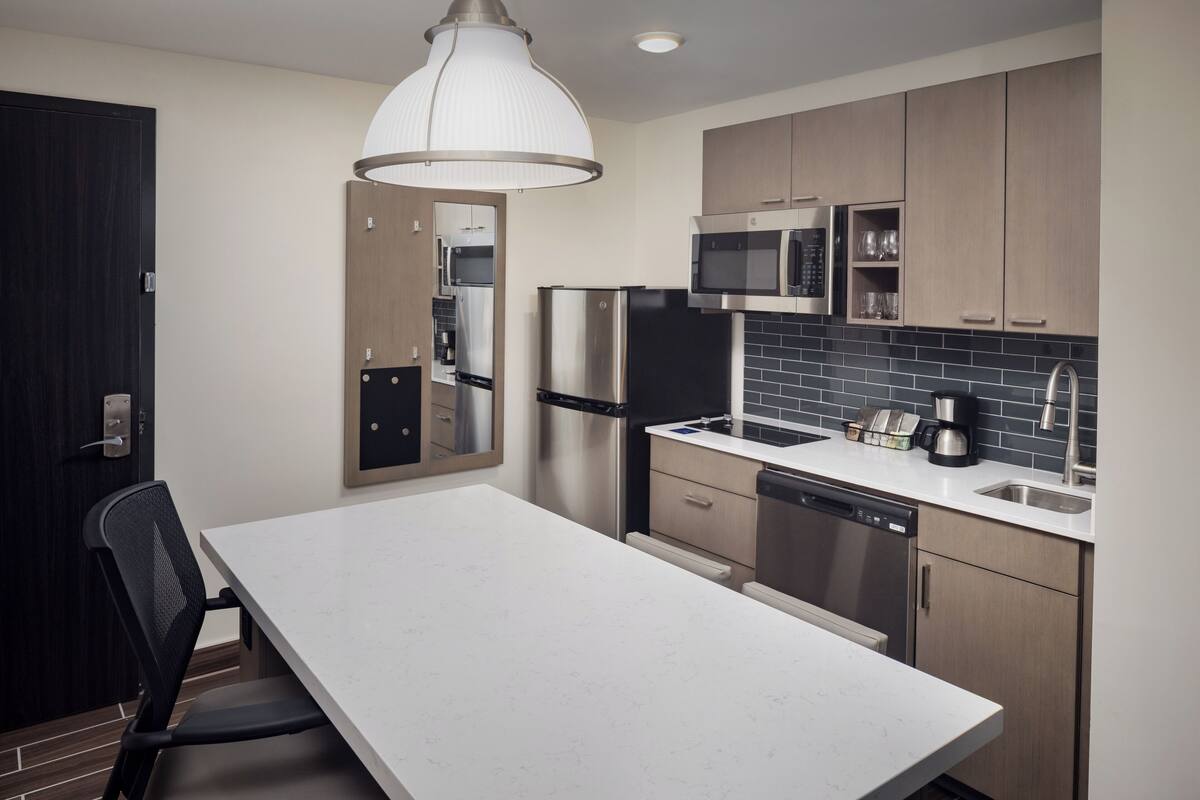 Una cocina moderna con electrodomésticos de acero inoxidable, encimera blanca y muebles de madera.