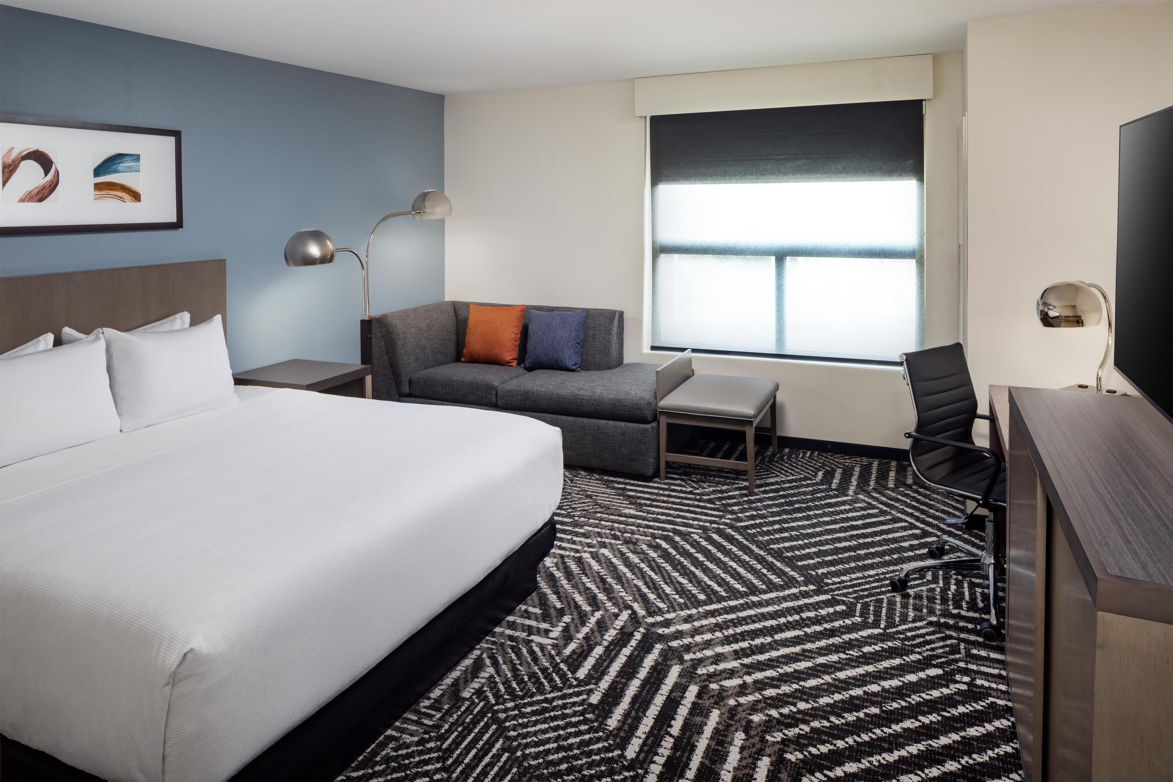 A hotel room with a large bed, a sofa, a desk, and a chair.