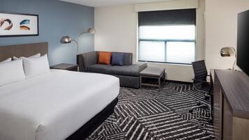 A hotel room with a large bed, a sofa, a desk, and a chair.