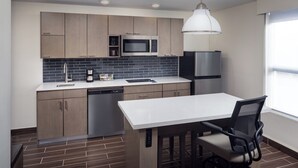 Una cocina moderna con armarios de madera, microondas, lavavajillas y un comedor con mesa y silla.