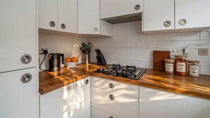 A kitchen with white cabinets, a gas stove, and jars of spices. - Canal View House | 2BR with Garden & Parking (London)