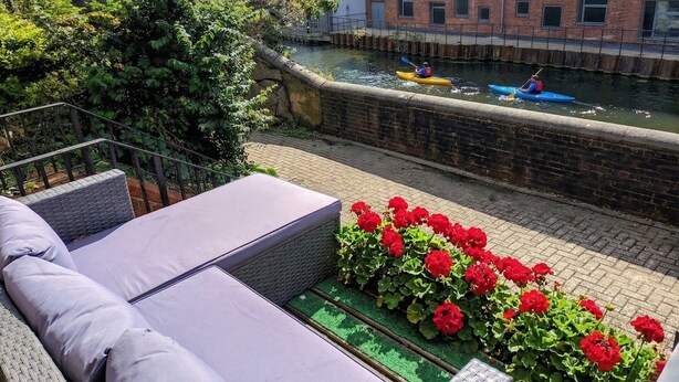 A riverside patio with outdoor seating and a view of a canal where kayakers are present. - Canal View House | 2BR with Garden & Parking (London)