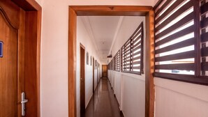 A long, narrow hallway with wooden doors and windows with horizontal blinds. - Beautiful Hotel In Greater Accra Region 1 (Oshiyie)