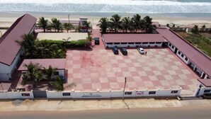 A beachfront hotel with a checkered parking area, palm trees, and a view of the ocean. - Beautiful Hotel In Greater Accra Region 1 (Oshiyie)