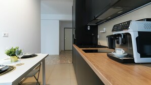 Eine moderne Küche mit integrierter Kaffeemaschine, einer weißen Arbeitsplatte und einem Essbereich mit Tisch für zwei Personen.