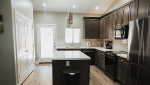 A modern kitchen with dark wood cabinets, a stainless steel refrigerator, and a central island with a black trash bin. - Cougar Canyon Unit A (Heber-Overgaard)