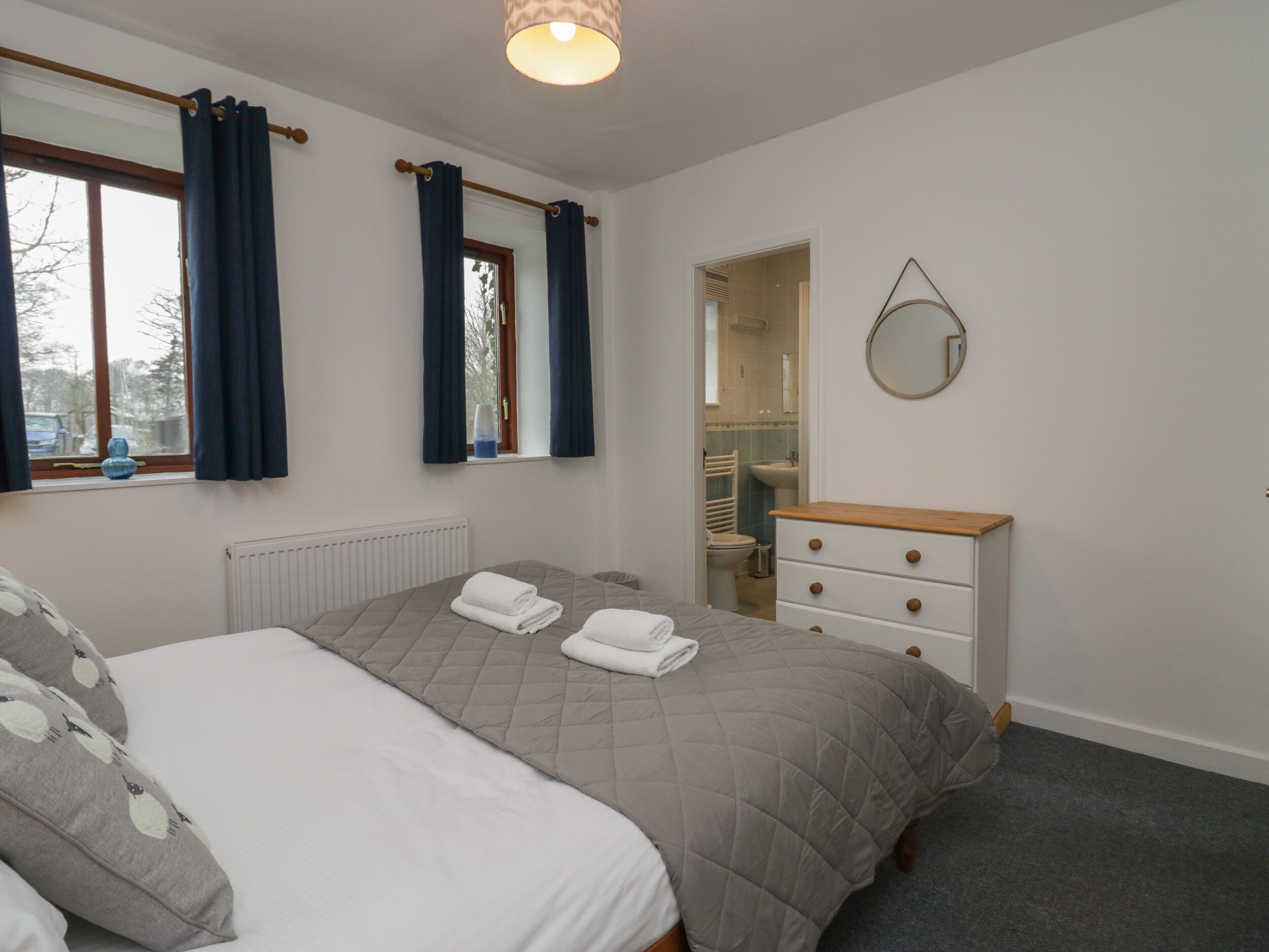 Une chambre à coucher avec un lit, une commode, un miroir et une fenêtre avec des rideaux.
