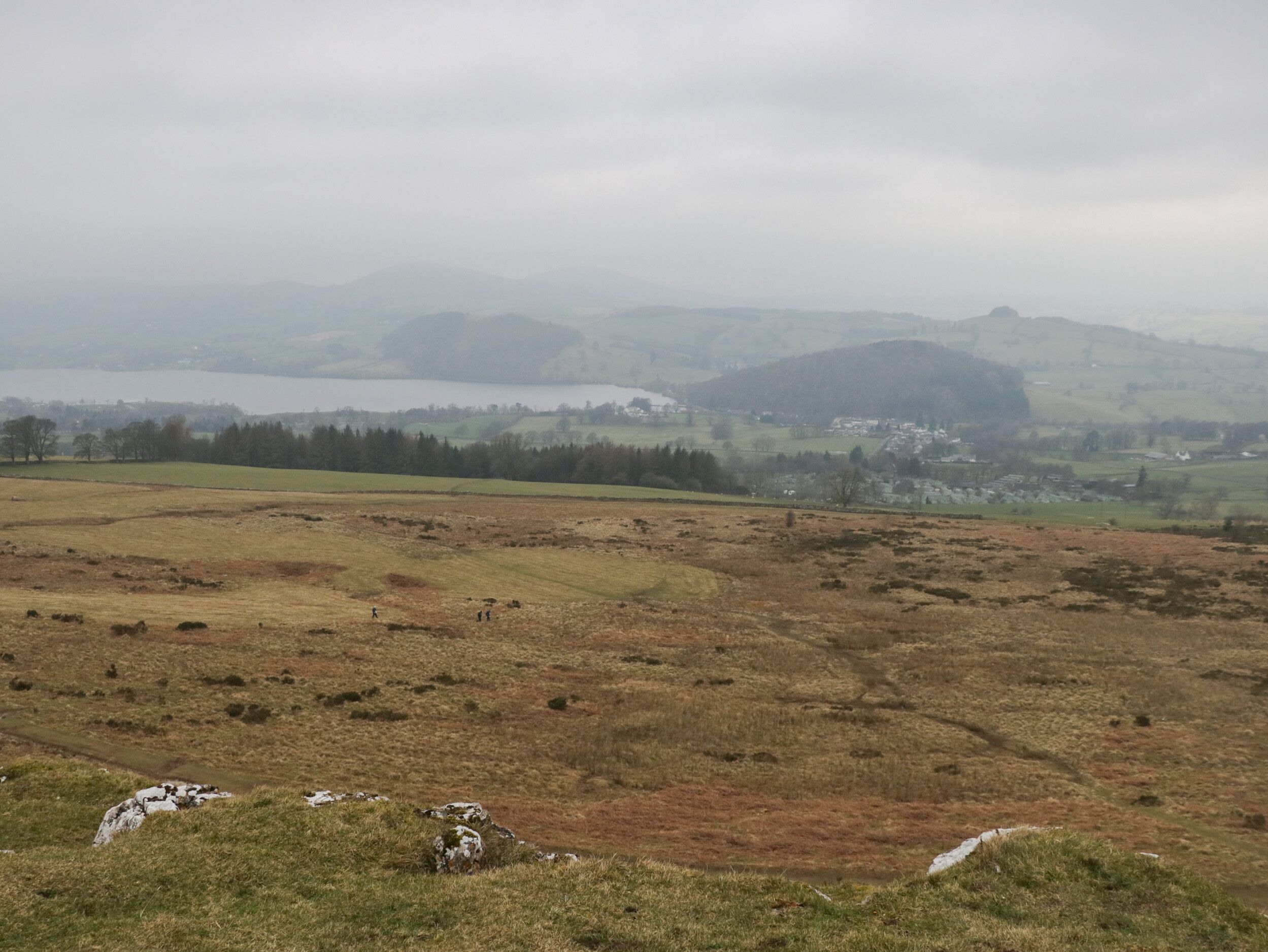 Vista panorámica de un paisaje montañoso con un lago y edificios a lo lejos.