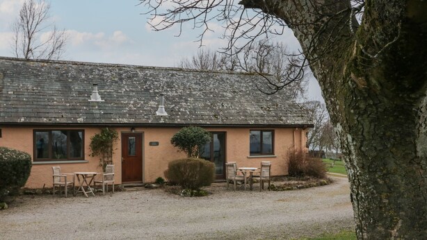 Une maison de plain-pied avec une allée gravillonnée, une porte d’entrée et une petite terrasse avec une table et des chaises.