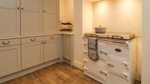 A kitchen with white cabinets, a clock on the wall, and an oven with a pot on top. - Riverdale House (Skipton)