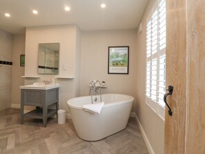 A bathroom with a freestanding bathtub, a vanity with a mirror, and a framed picture on the wall.