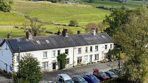 A white building with multiple windows and a flat roof, located in a rural area with green fields and a stone wall in the background. - Riverdale House (Skipton)