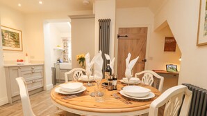 A dining area with a round wooden table set for four, surrounded by white chairs with floral upholstery. - Riverdale House (Skipton)