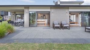 A modern house with a patio, a dining area, and a kitchen visible through glass doors.