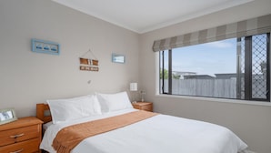 A bedroom with a large bed, wooden nightstands, a window with a view, and wall decorations.