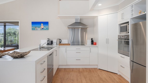 A modern kitchen with white cabinetry, stainless steel appliances, and a wooden floor.