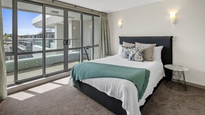 Ein modernes Hotelzimmer mit einer großen Schiebeglasdoor zum Balkon, einem ordentlich bezogenen Bett mit einer grünen Tagesdecke und einem kleinen runden Tisch.