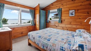 Un dormitorio con techo de madera, una cama con colcha a cuadros, una mesita de noche, un escritorio y una ventana con cortinas.