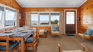 Una cabaña de madera con zona de comedor, un sofá y una silla con vistas al mar.