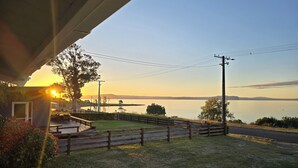 Vista de un lago al atardecer, con una terraza de madera y una casa en primer plano.