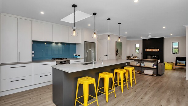 A modern kitchen with white cabinets, a central island with bar stools, and pendant lighting. - Seaside Escape - Ruakaka Holiday Home (Ruakaka)
