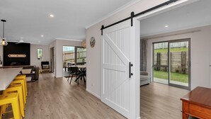 A spacious kitchen with a dining area, a sliding barn door, and a view of the backyard. - Seaside Escape - Ruakaka Holiday Home (Ruakaka)