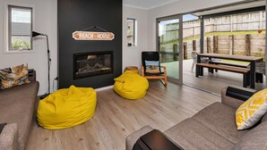 A modern living room with a fireplace, yellow bean bags, and a sign reading "Beach House". - Seaside Escape - Ruakaka Holiday Home (Ruakaka)