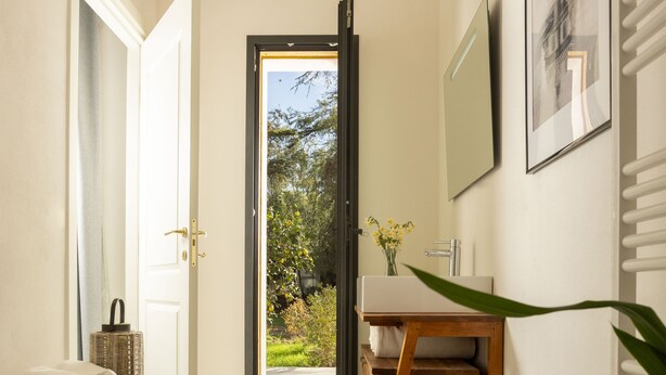 A modern bathroom with a large white bathtub, a wooden vanity, and a view of a garden through an open door. - Dèpendance - Lequile - Alfa Country House (Lequile)