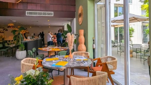 A modern interior with a round dining table surrounded by wicker chairs, a large vase, and a hanging light fixture.