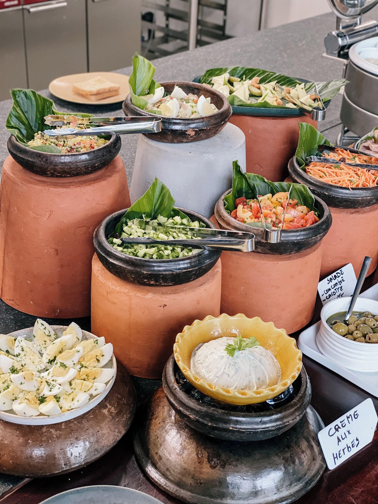 Un bufé con diversos platos servidos en vasijas de barro tradicionales, entre ellos ensaladas, verduras y un plato cremoso.