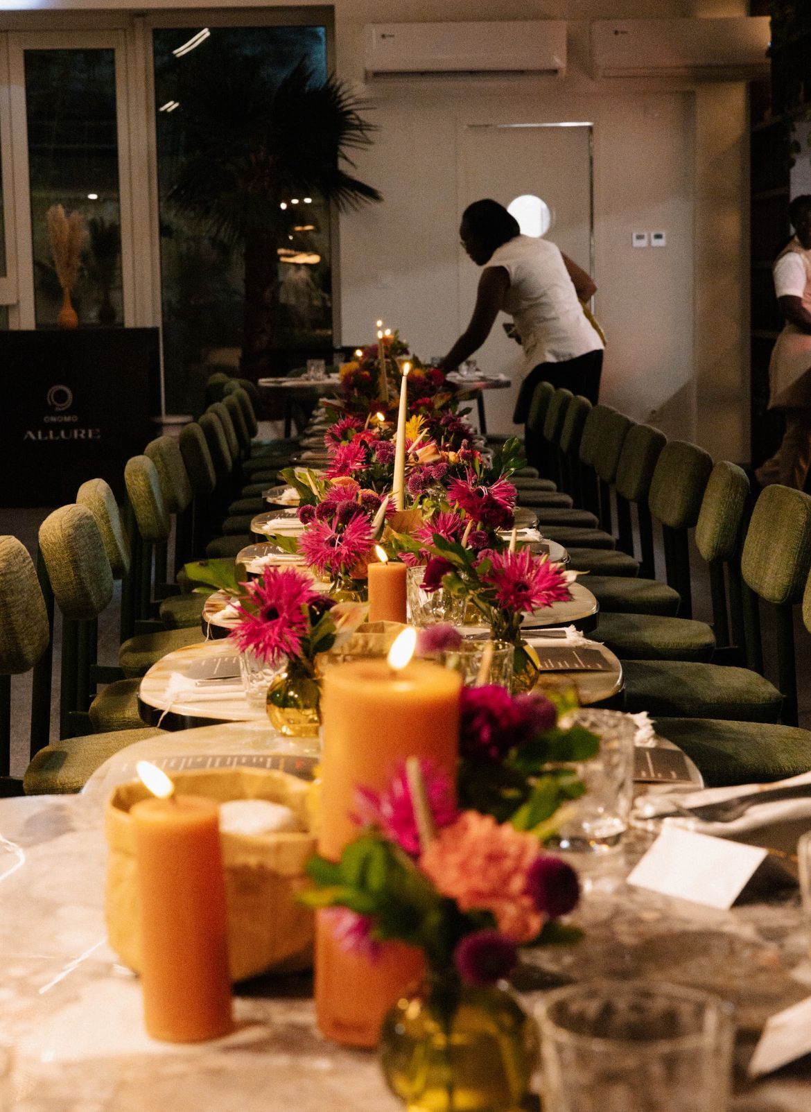 Une longue table à manger, décorée de bougies, de fleurs et de verres, probablement dans un restaurant ou une salle de réception.