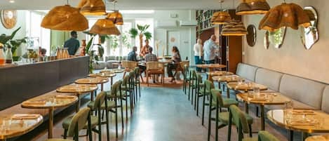 Ein Restaurant mit runden Tischen, grünen Stühlen, einer Bar und hängenden Korbtischen.
