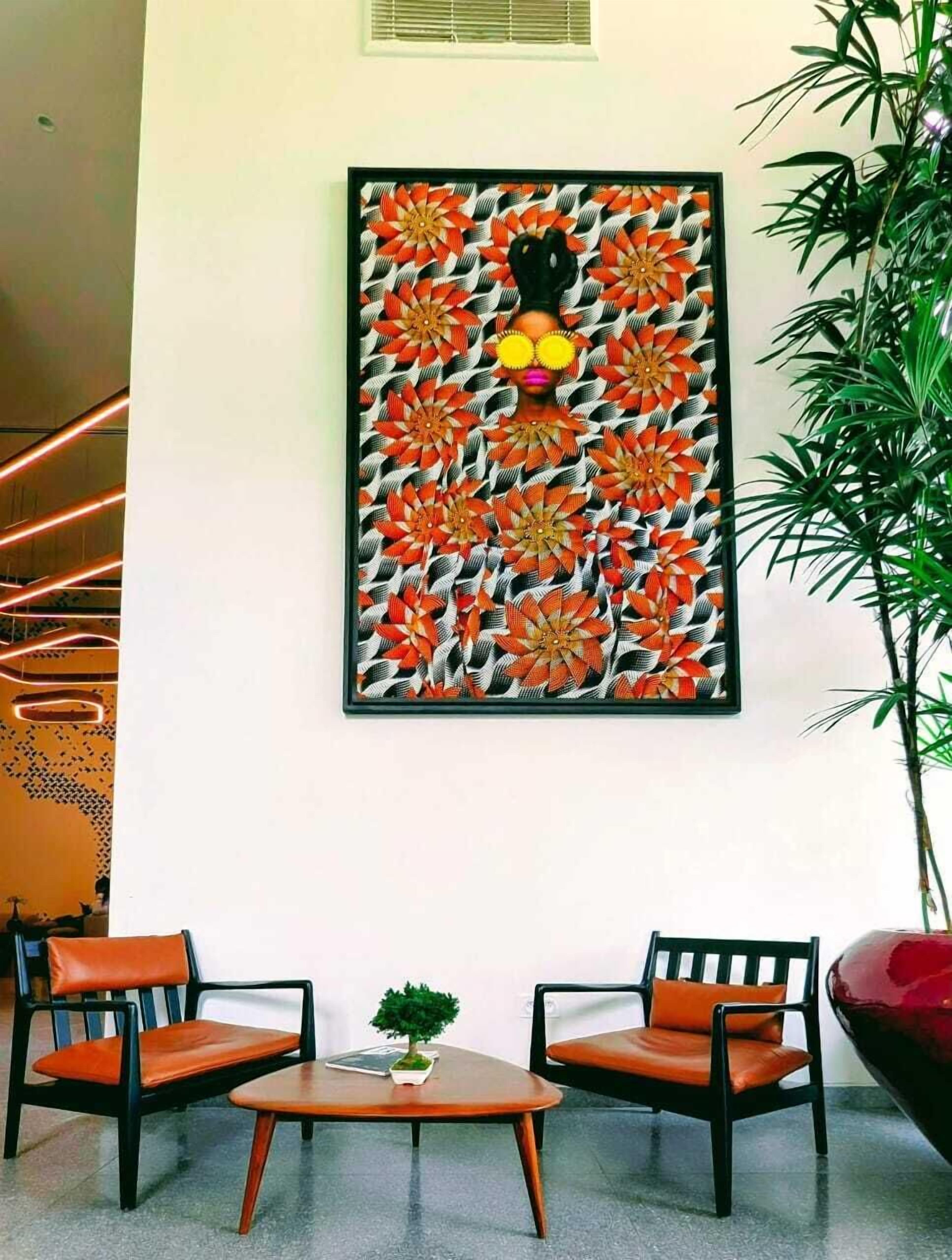 A modern interior with a wall-mounted artwork featuring a stylized floral pattern, two wooden chairs with orange cushions, and a small table with a plant.