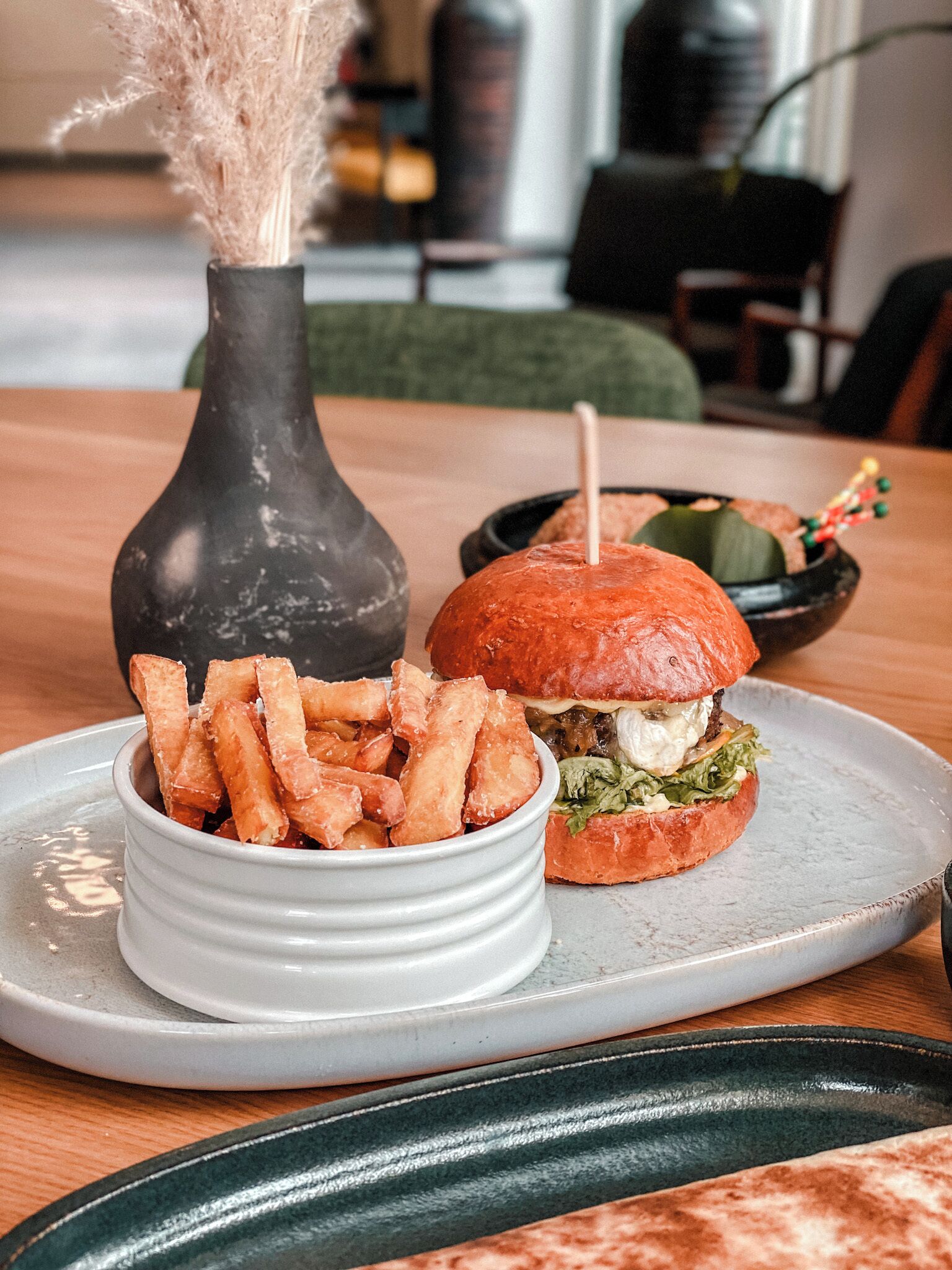 Une table à manger avec une assiette de frites, un hamburger et un vase décoratif.