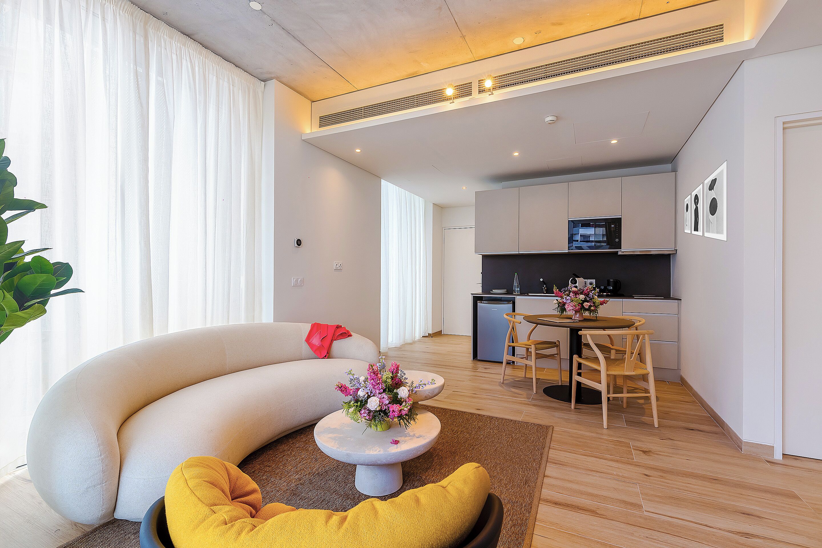 Ein modernes Wohnzimmer mit einer gebogenen Couch, einem kleinen runden Tisch mit floralem Mittelstück und einem gelben Kissen.