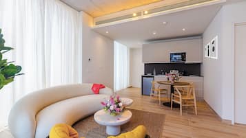 Ein modernes Wohnzimmer mit einer gebogenen Couch, einem kleinen runden Tisch mit floralem Mittelstück und einem gelben Kissen.