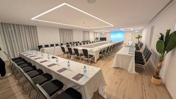 Sala de conferências com mesas compridas, cadeiras e garrafas de água.