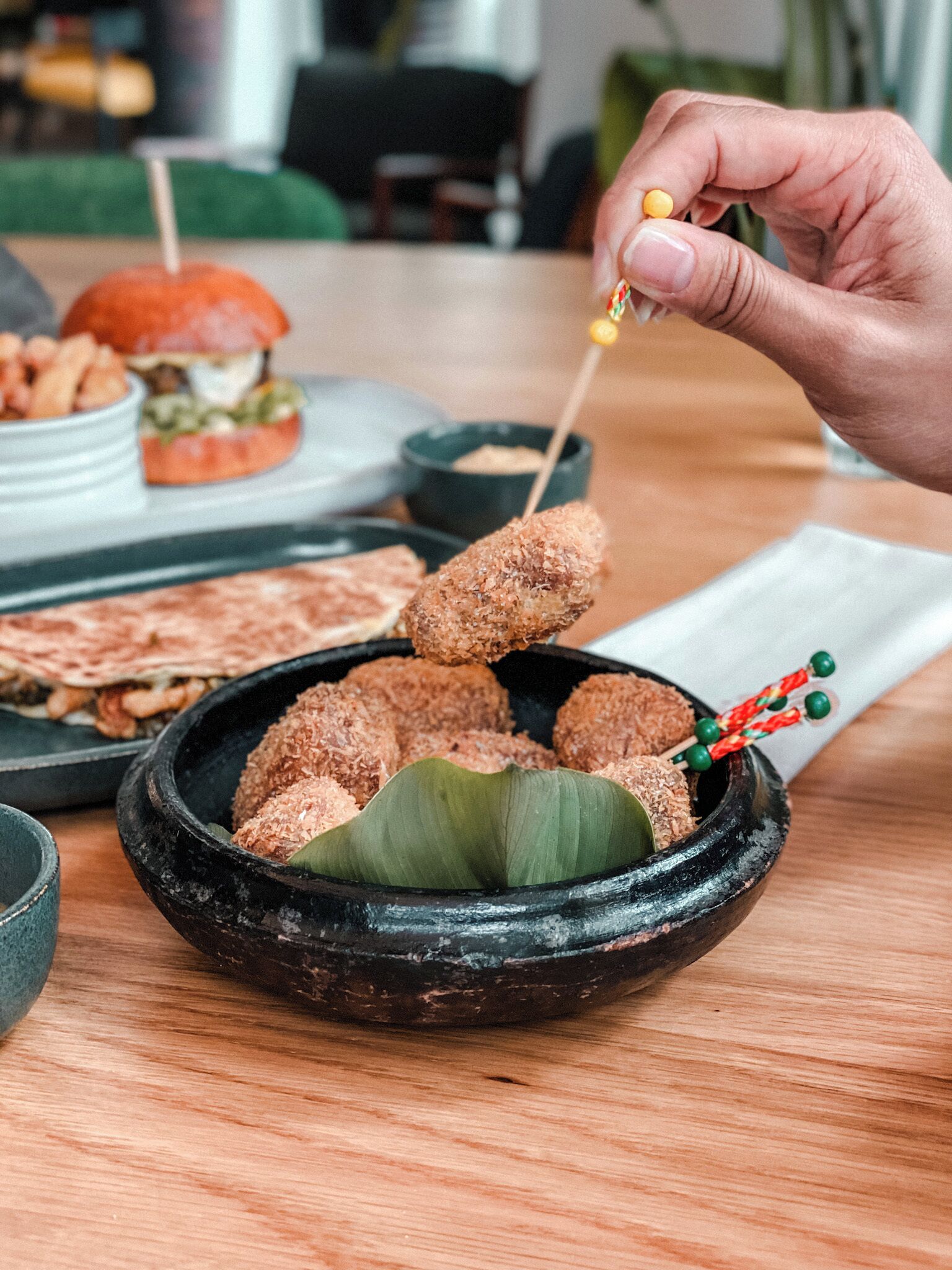 A hand holding a skewer with food items over a black bowl with food in it.