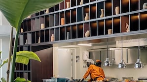 A modern kitchen with a chef preparing food, surrounded by shelves of decorative pottery.