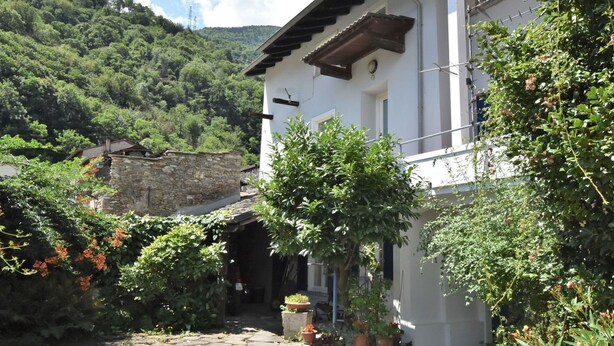 A stone-paved courtyard with a white building featuring a wooden balcony and potted plants. - Beautiful private villa for 6 guests with WIFI, A/C, TV, patio and pets allowed (Cosio Valtellino)