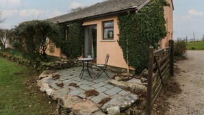 A cozy cottage with a stone patio, a wooden gate, and a small table and chair set outside. - Winder Green (Penrith)