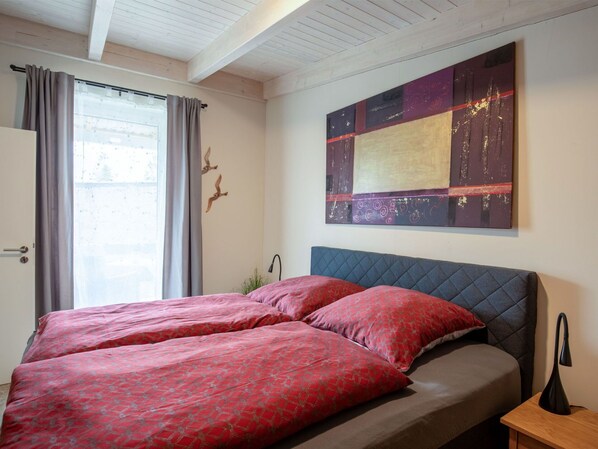 A bedroom with a bed, a nightstand, a wall-mounted artwork, and a window with curtains.