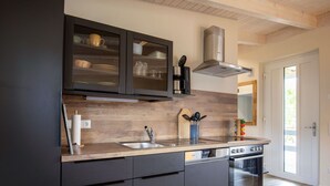 A modern kitchen with dark cabinetry, a wooden backsplash, stainless steel appliances, and a large window providing natural light. - Cosy apartment for 2 people with WIFI, TV and terrace (Osten)