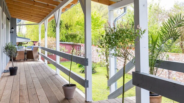 A covered outdoor area with a wooden deck, white railings, and potted plants. - Cosy apartment for 2 people with WIFI, TV and terrace (Osten)